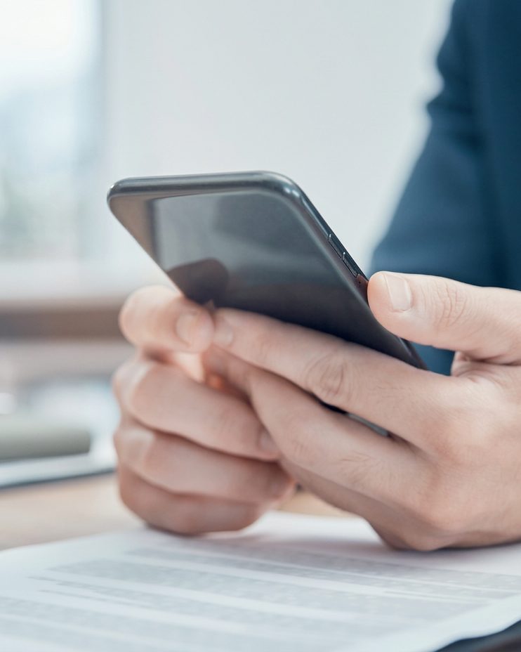 A person's hands holding a phone at a desk, the screen out of focus