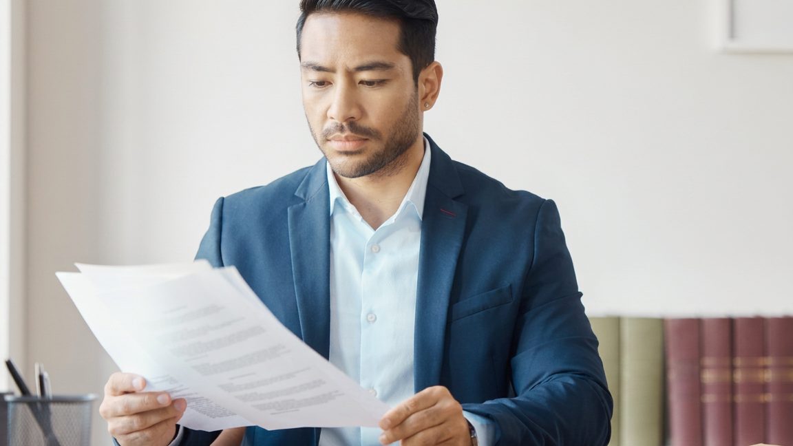 An attorney reading a printed document at a desk, law books out of focus behind him